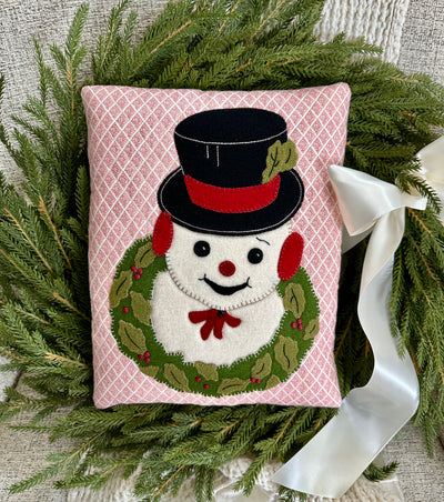 Decorative pillow with a snowman design peek through a wreath